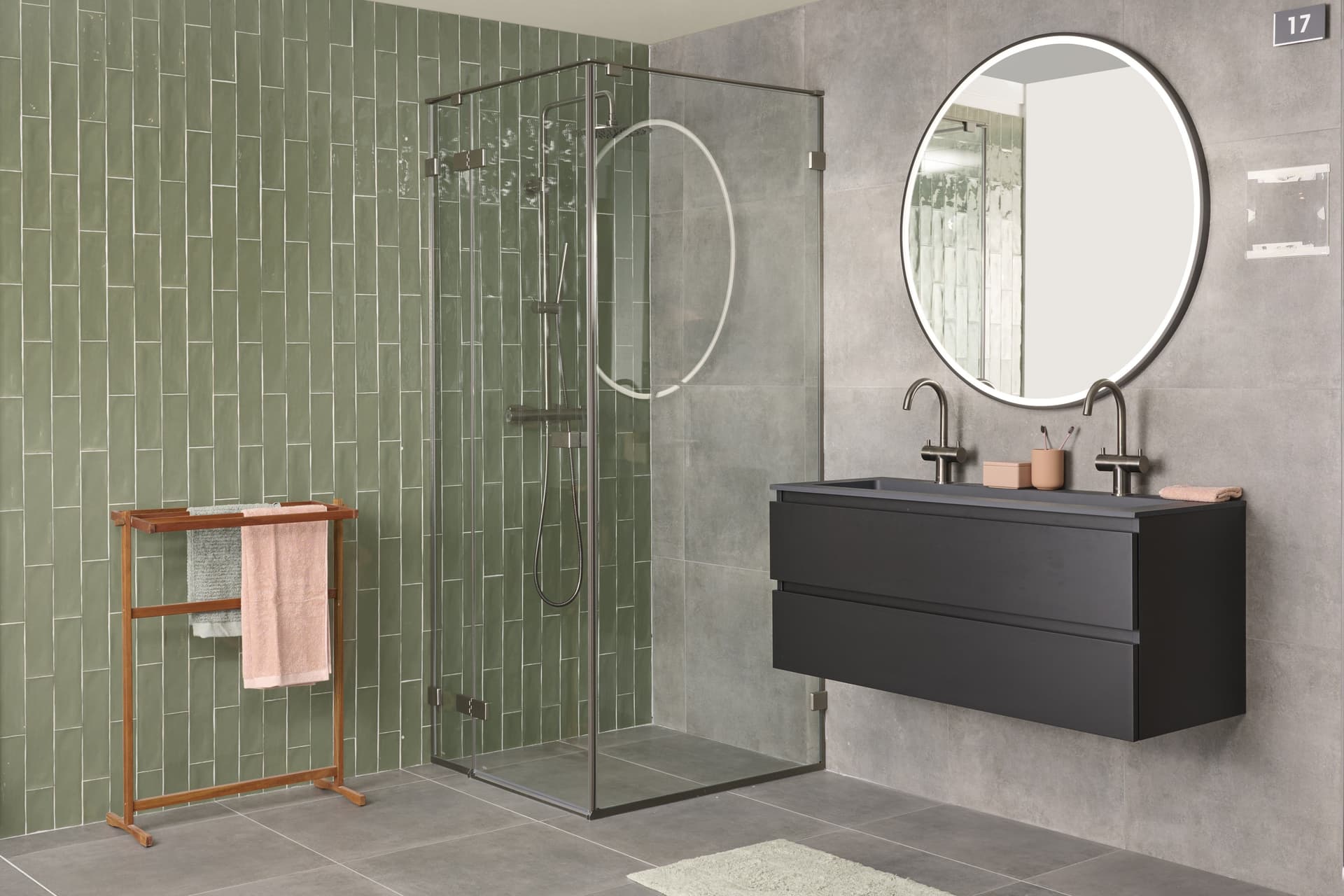 Badkamer met groene tegelmuur, grijze vloer en zwart meubel met ronde spiegel