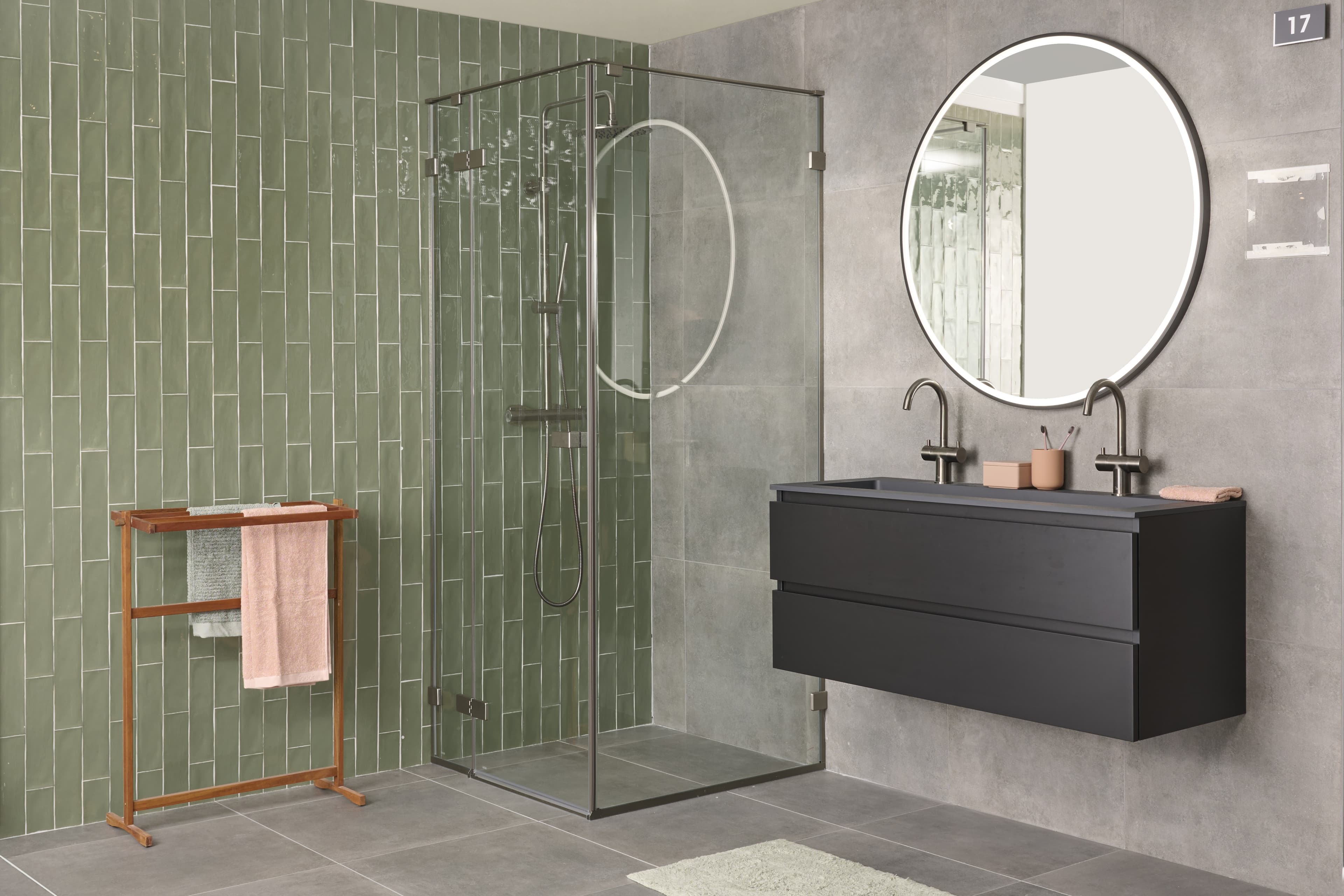 Badkamer met groene tegelmuur, grijze vloer en zwart meubel met ronde spiegel