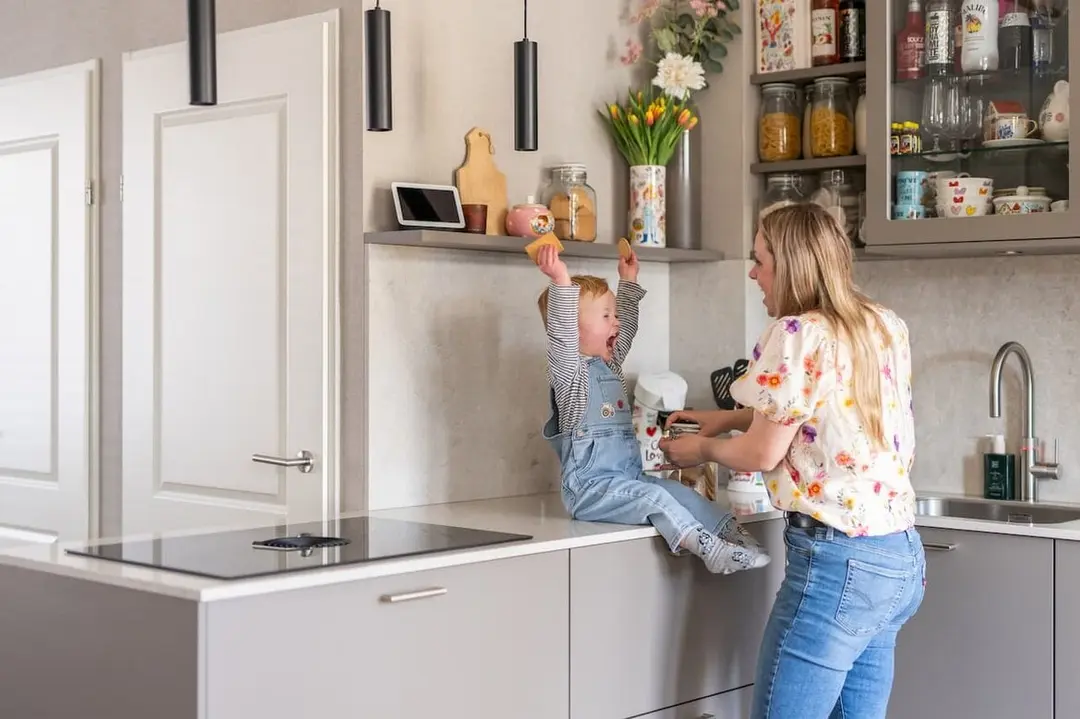 Grijze hoekkeuken waar moeder en haar zoontje op de aanrecht koekjes aan het eten zijn