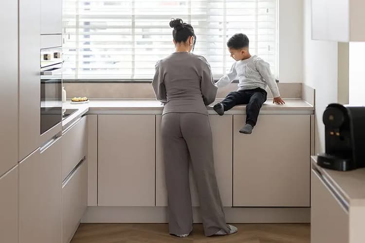 Beige hoekkeuken waar een jongetje op de aanrecht en zijn moeder iets aan het klaarmaken is